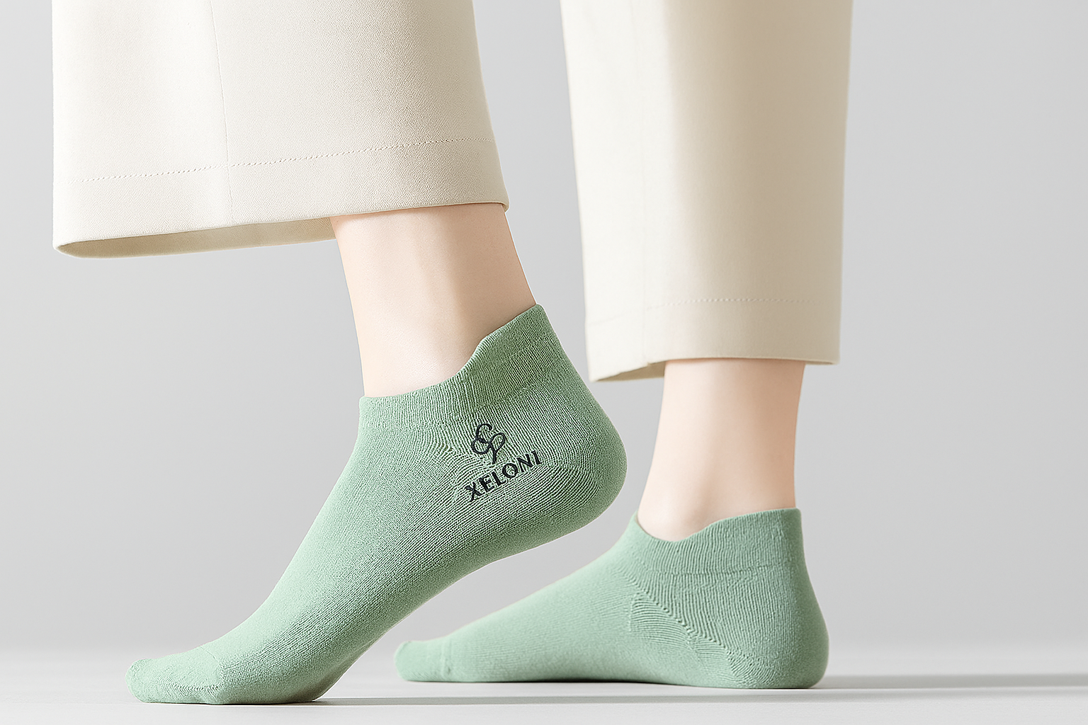 Close-up of a woman wearing light green cotton ankle socks embroidered with the black XELONI logo.